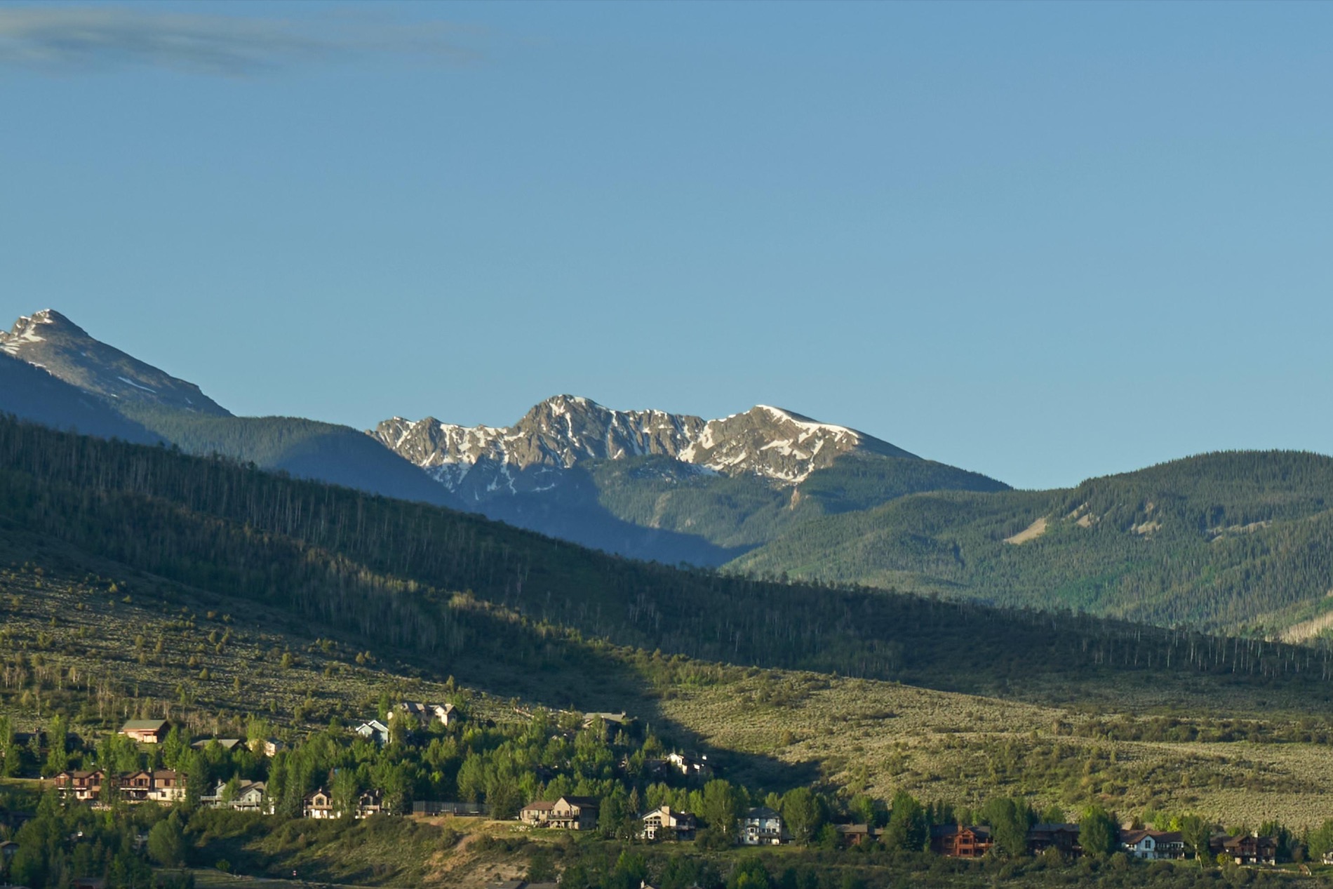 Snowcapped Colorado peaks above forested foothills and a mountain town at golden hour