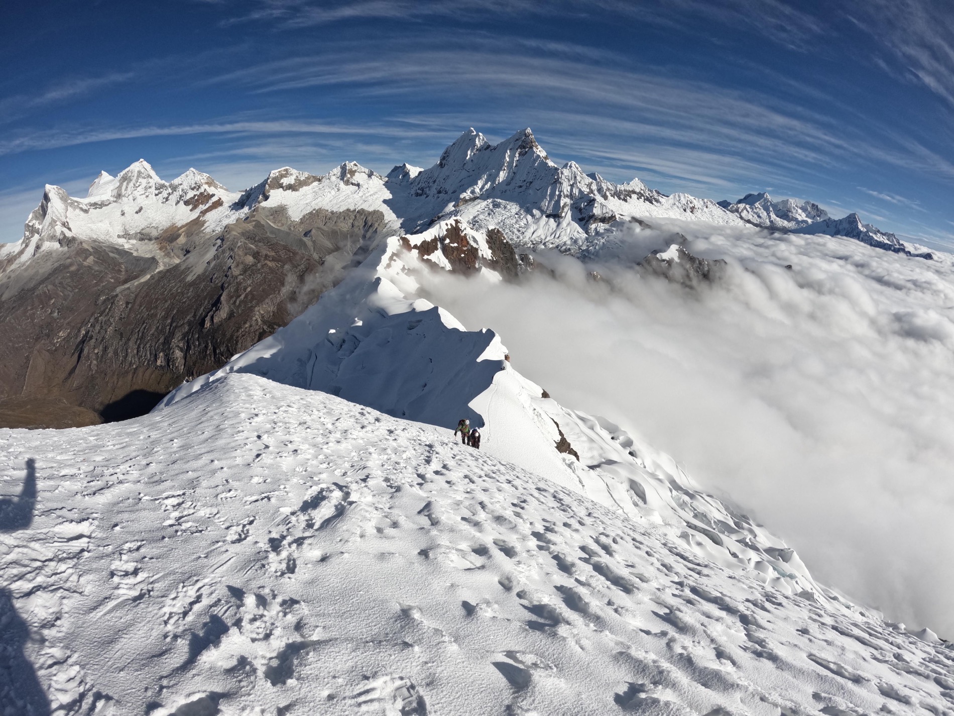 Two mountaineers ascending a snowy summit ridge above a sea of clouds in the Cordillera Blanca, Peruvian Andes