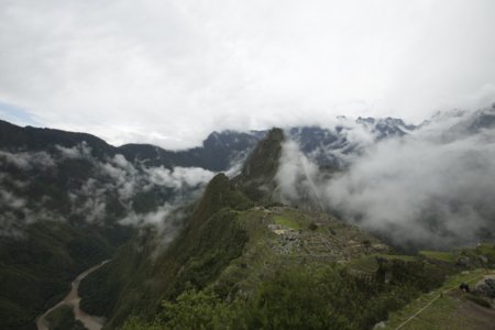 Cloud-shrouded green ridge of Machu Picchu terraces above a winding river canyon