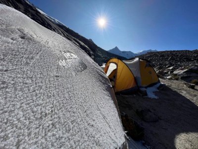 Orange mountaineering tent on snow-streaked slope, bright sun in deep blue sky; by Alexander Estrada