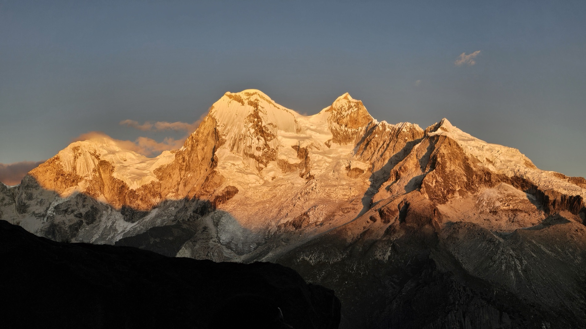 Golden sunrise light strikes the snow and glaciers of a high Andean peak against a clear blue sky.