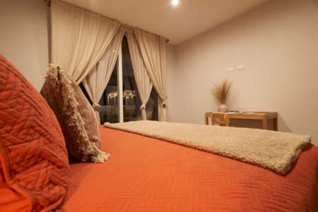 Bedroom corner with orange-toned bed, throw pillows and curtained balcony at night