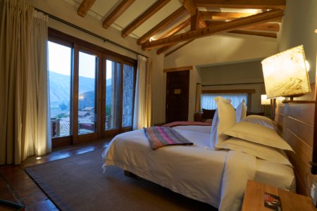 Mountain-view suite with timber-beam ceiling, white linens and glass balcony doors