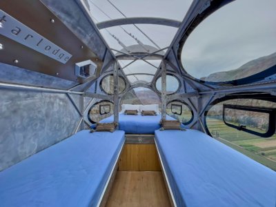 Interior of transparent Skylodge capsule with twin and double beds over a green valley