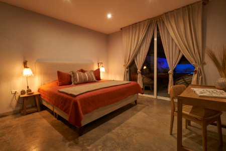 Bedroom at night with orange bedspread and glass doors revealing a blue-lit pool, shot by Alexander Estrada