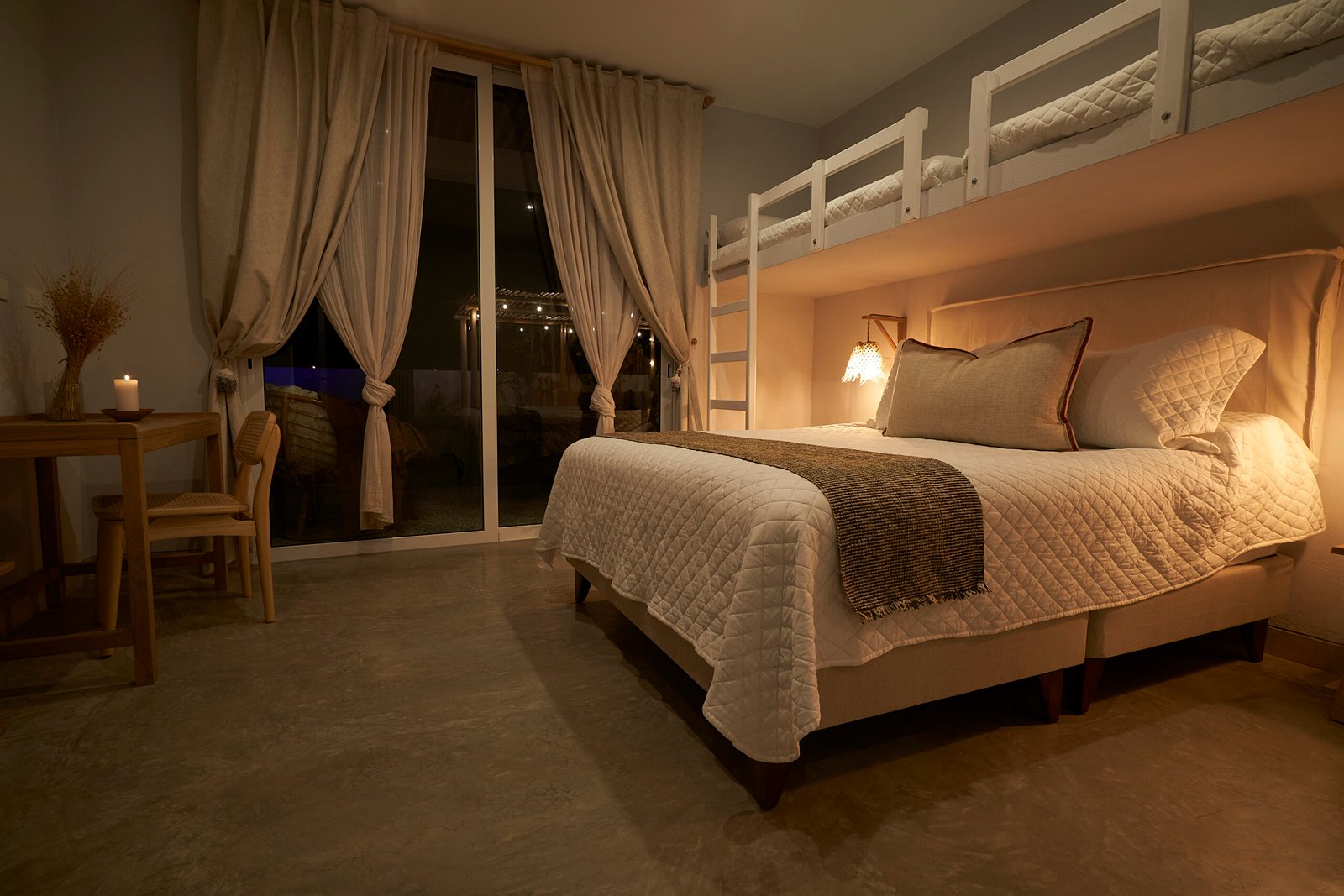 Casa Raiz bedroom with twin white loft bunks framing a queen bed under warm sconces