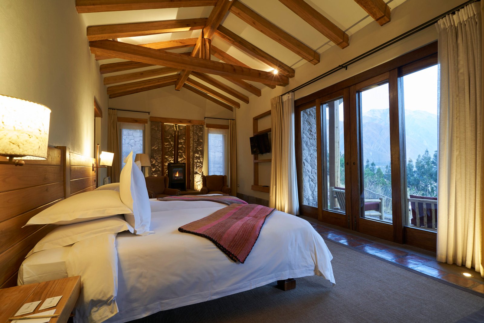 Mountain lodge suite with vaulted wood ceiling, fireplace and panoramic valley windows, by Alexander Estrada